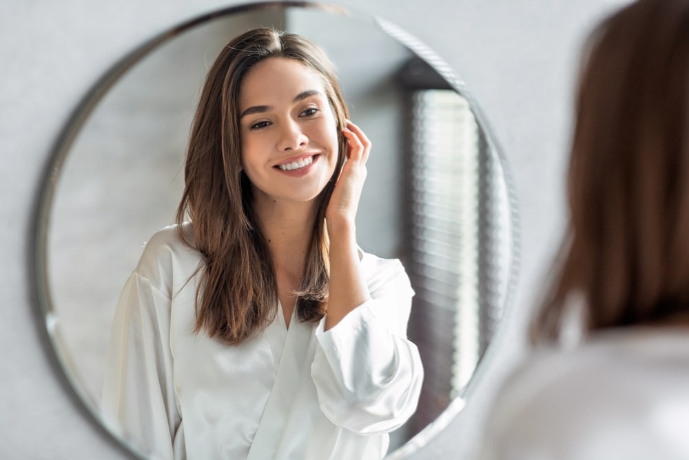 Portrait Of Attractive Happy Woman Looking At Mirror In Bathroom